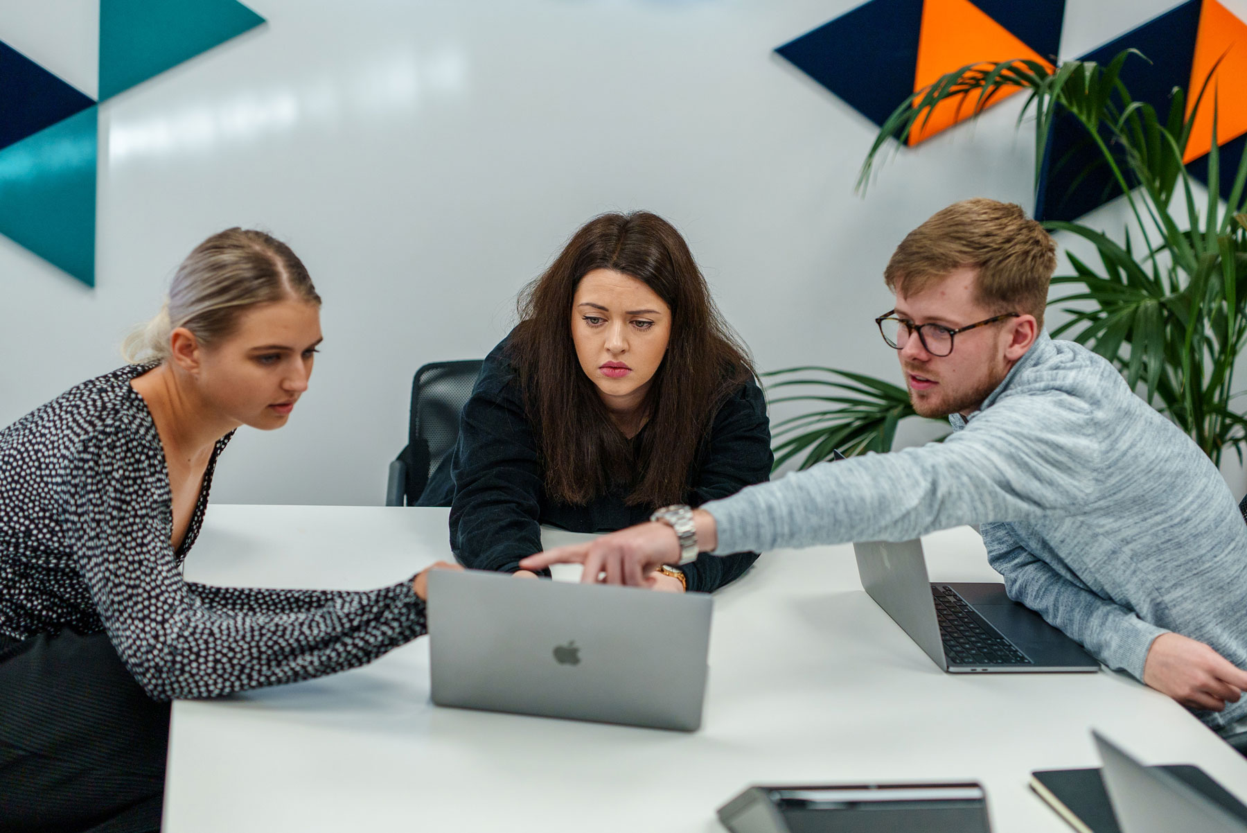 Three people are pointing at a laptop screen