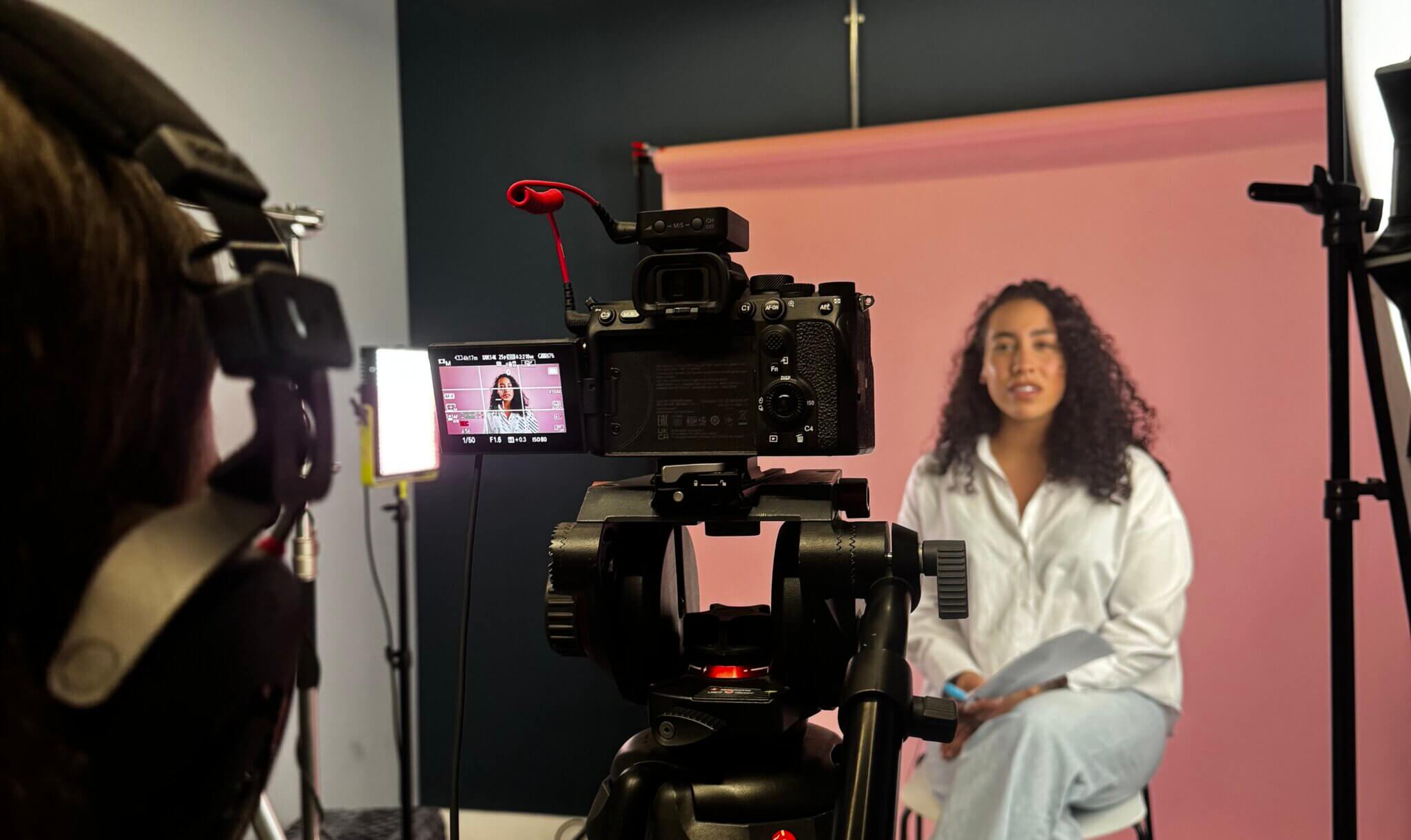 Woman sat filming a video behind large studio lights