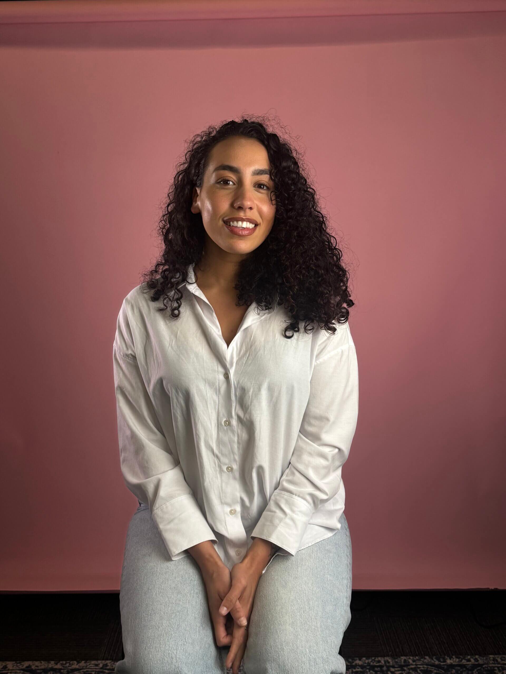 Women sat on a stool in front of a pink background