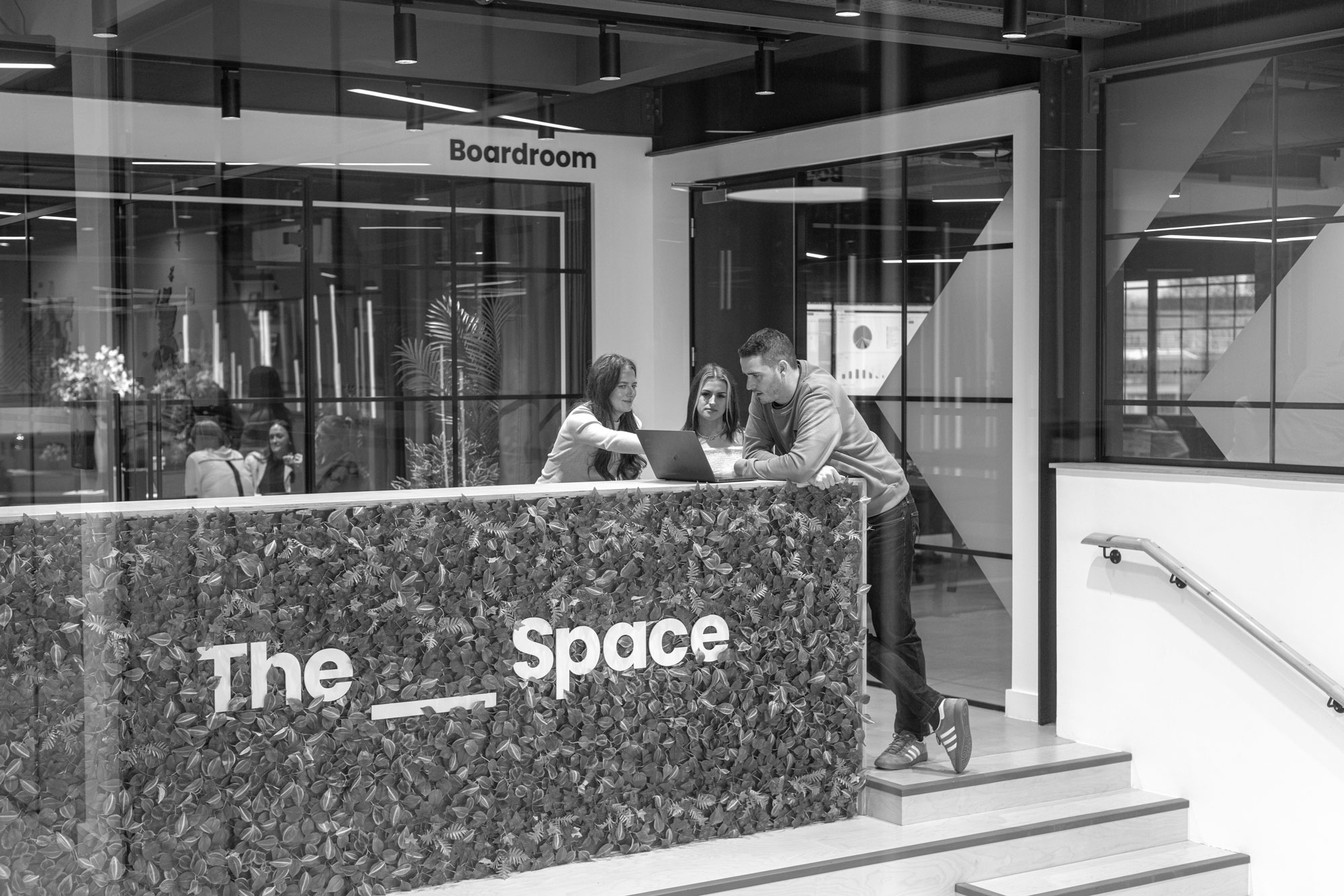 A group of people is stood at the top of presentation stairs looking at laptop