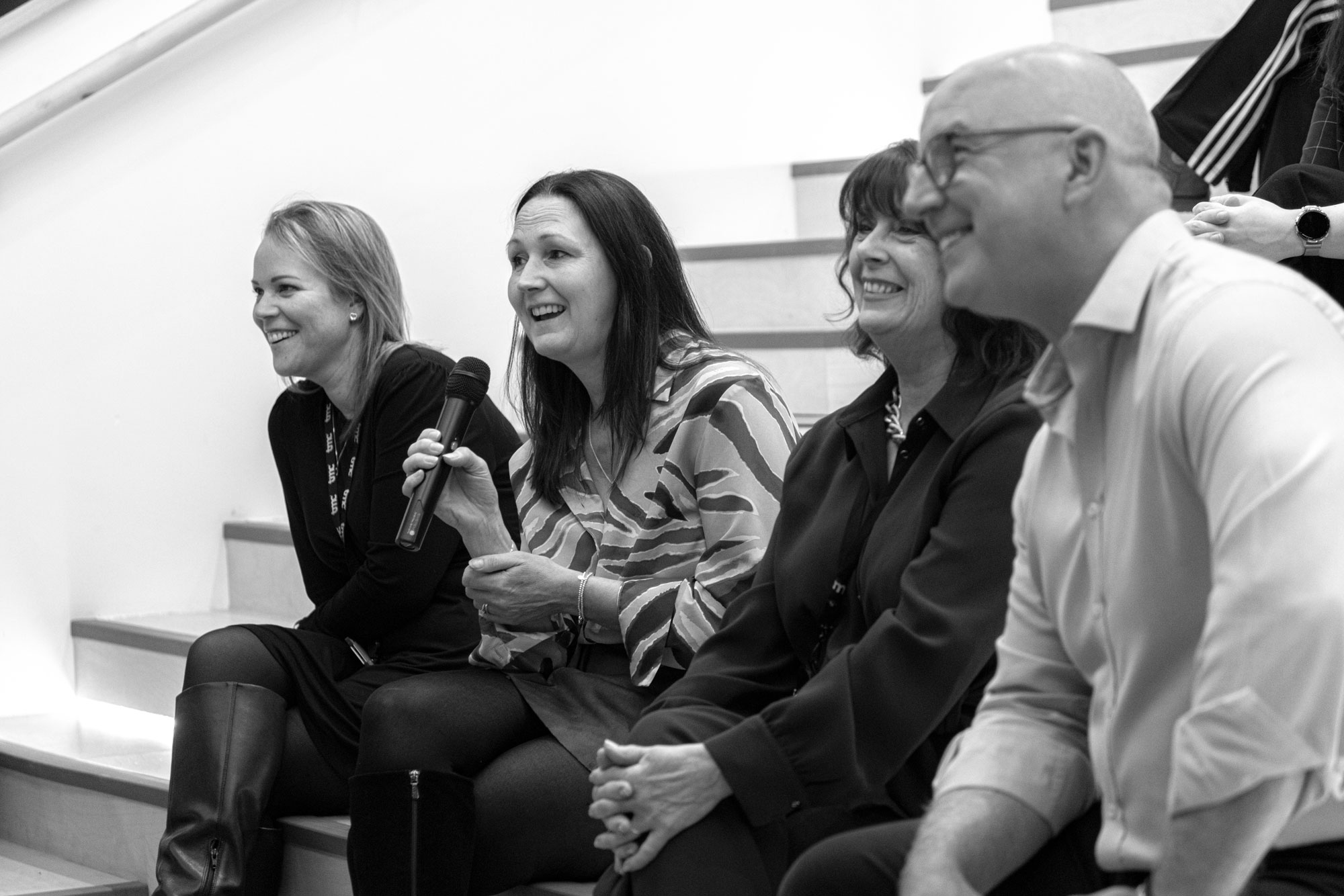 Women is speaking into mic, sat on presentation steps with others