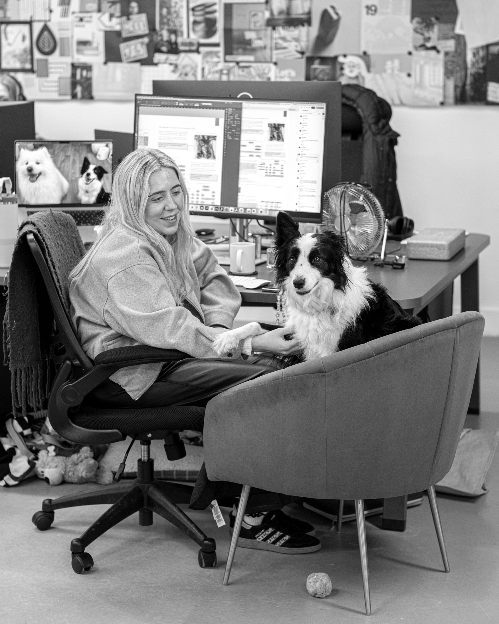 Woman is sat at desk with dog on a chair next to her